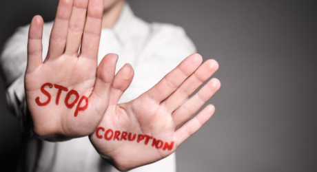 Image of a person in a white shirt with a close up of hands that say stop corruption. 